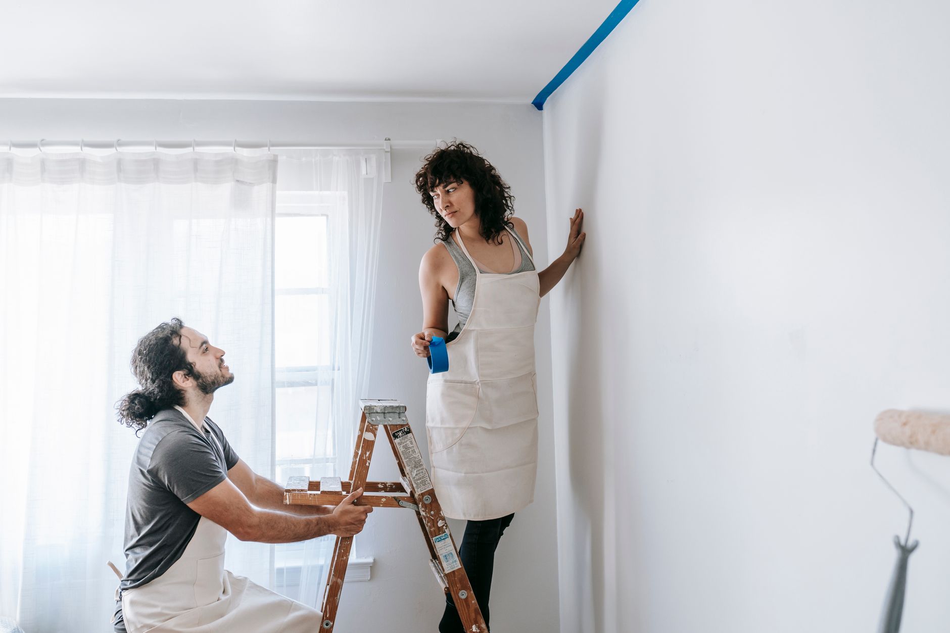 A couple in aprons working together on room renovation using paint rollers indoors in Santa Monica, CA