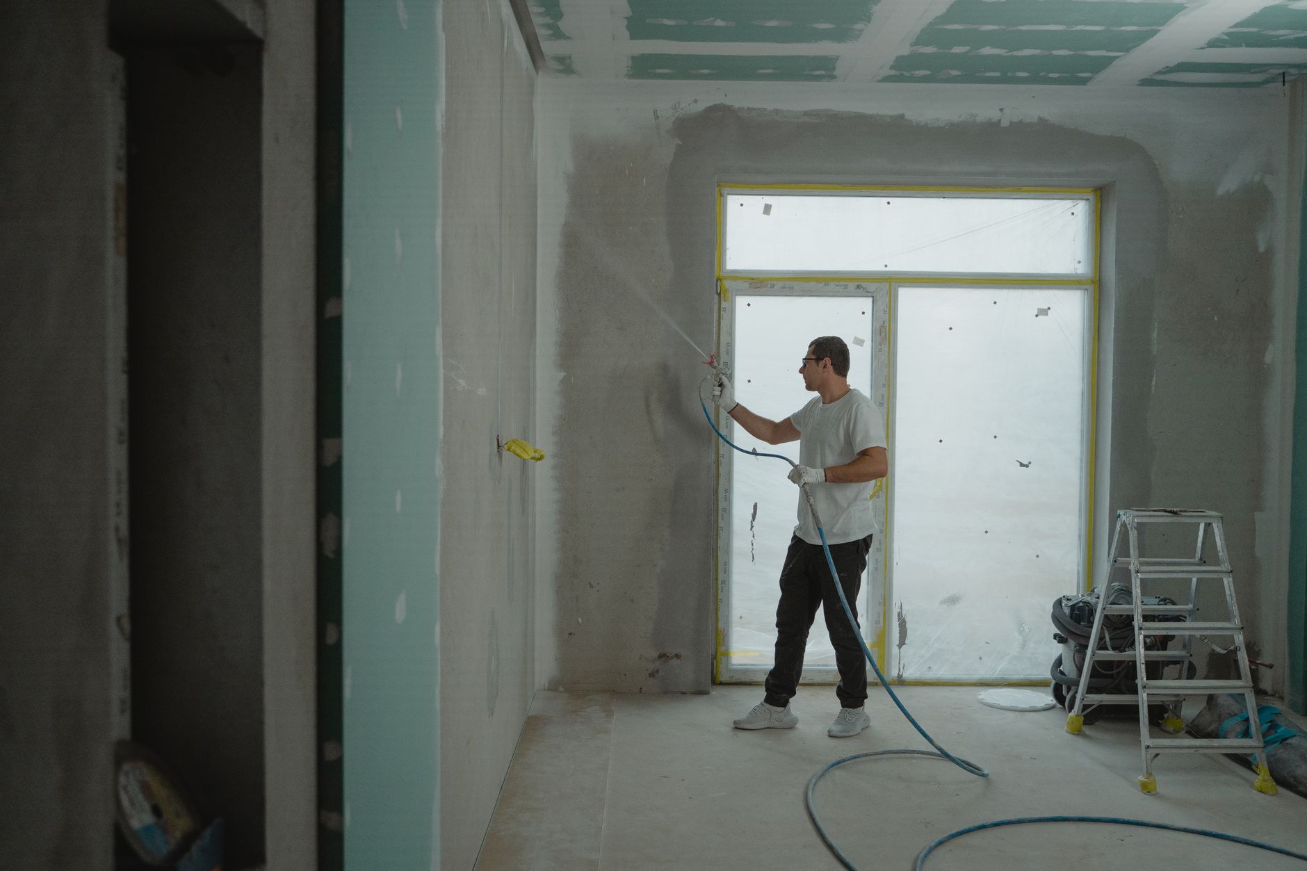 A man sprays paint on a wall while renovating an indoor room with professional equipment in Santa Monica, CA